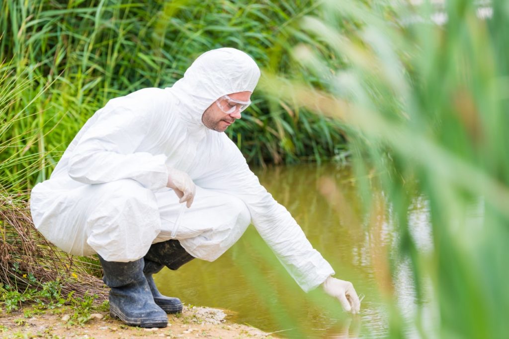 Man in hazmat suit examining a water sample at a stream for a PFAS lawsuit