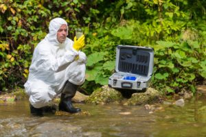Man in hazmat suit examining a water sample at a stream for a PFAS lawsuit
