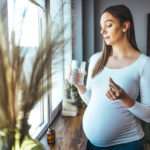 Pregnant woman in gray taking medication with water